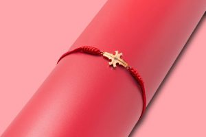 Photo of a red string JUN bracelet with a gold cross.
